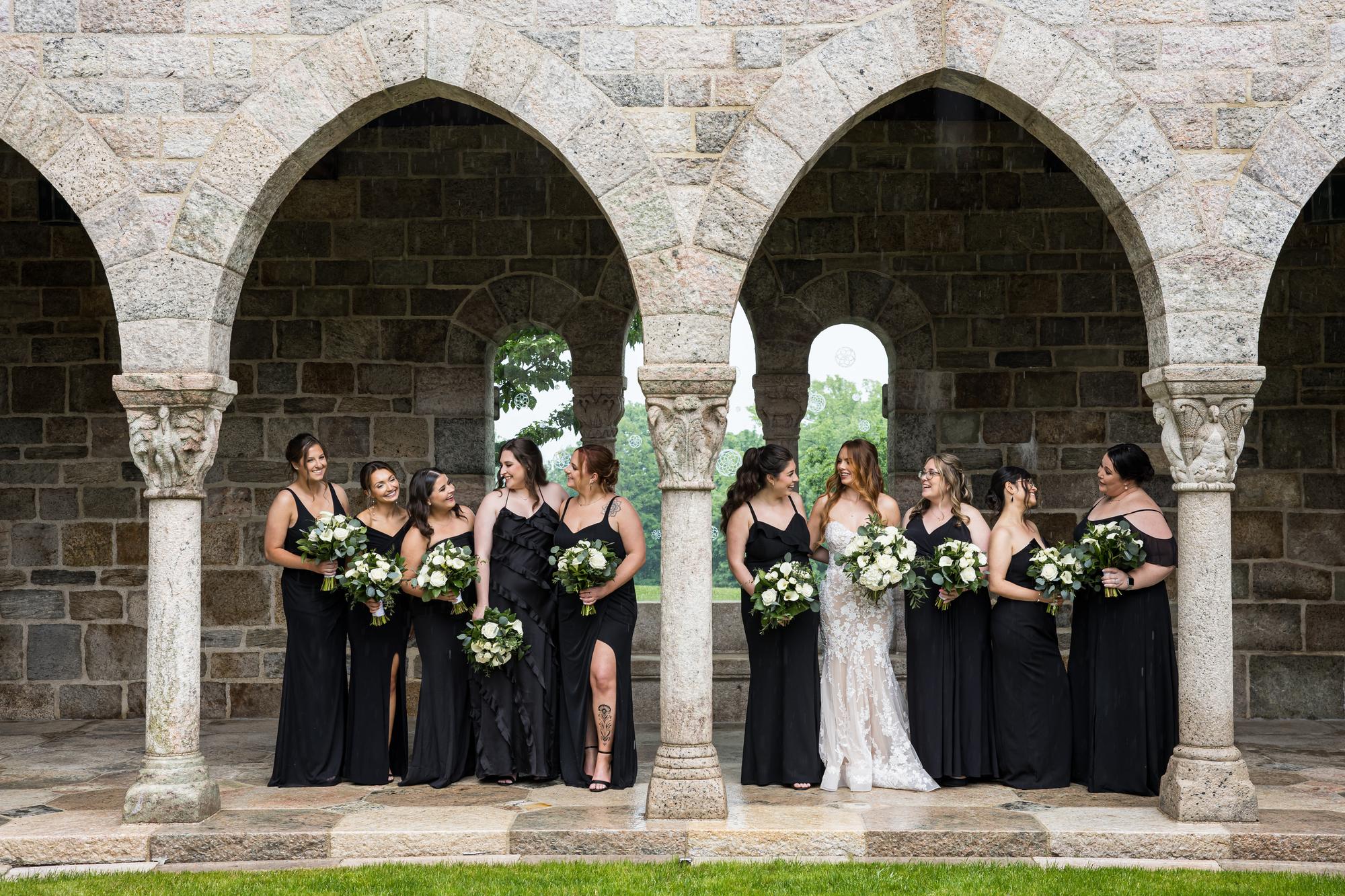 Bride and her bridesmaids under the stone arches at Glencairn Museum, Bryn Athyn, Montgomery County